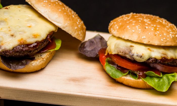 Ricetta Emmental Classico cheeseburger con formaggio Emmental di GOLDSTEIG, carne macinata, lattuga e pomodoro su una tavola di legno 