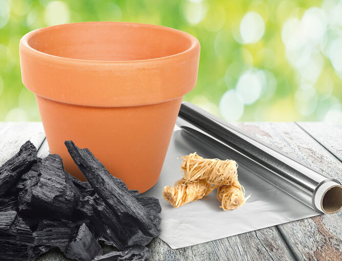 Barbecue realizzato con un vaso da fiori, un foglio di alluminio, un accendino di legno e carbonella su un tavolo di legno per grigliare i prodotti GOLDSTEIG