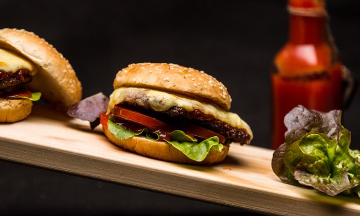 Ricetta Emmental Classico cheeseburger con formaggio Emmental di GOLDSTEIG, carne macinata, lattuga e pomodoro su una tavola di legno 