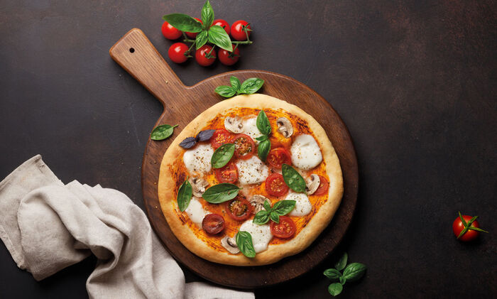 Cosa significa fior di latte: Una pizza con mozzarella fior di latte, foglie di basilico, pomodori e funghi adagiata su una tavola di legno.