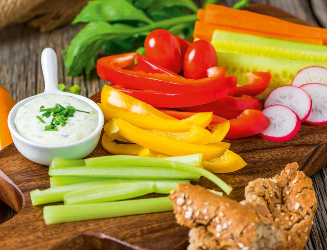 Spuntino con bastoncini di verdure, pane e salsa su un tagliere di legno