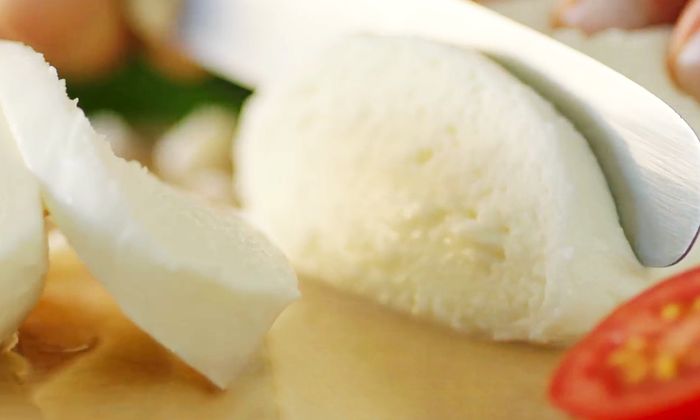 Coltello che taglia una palla di mozzarella di GOLDSTEIG su una tavola di legno - un formaggio a pasta filata