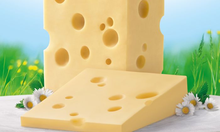 Fetta di Emmental di GOLDSTEIG senza crosta con margherite davanti a un prato fiorito